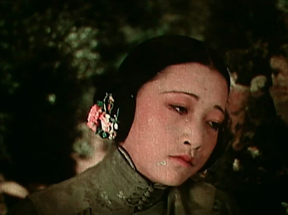 Anna May Wong in close-up in The Toll of the Sea, in colour: her head tilted, eyes lowered, a spray of pink flowers over her ear.