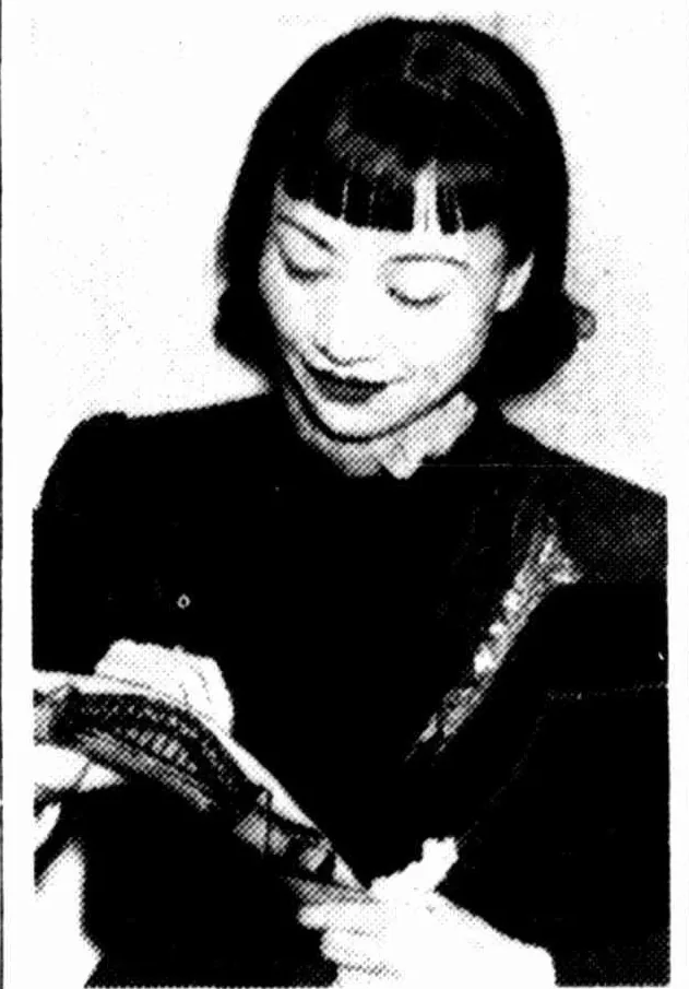 Anna May Wong smiling down as she signs a boomerang.