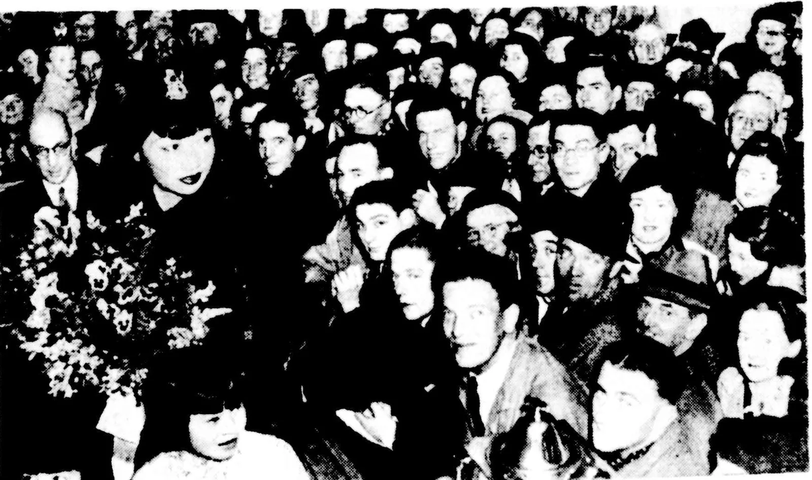 A packed crowd of men in hats in Bourke Street, Anna May Wong in a turban among them with a bouquet.