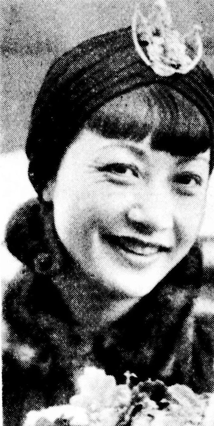 Anna May Wong smiling broadly in a close turban and fur collar, above a large bouquet.